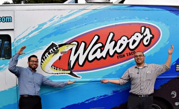 Two men posing in front of a Wahoo's food truck